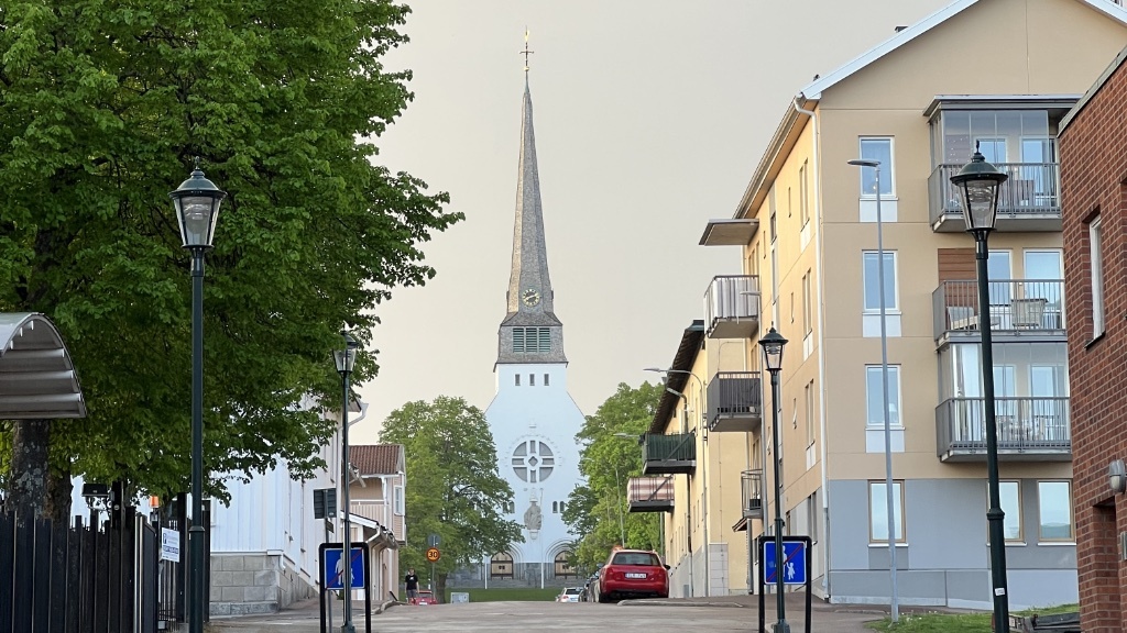 En lugn gata leder mot en kyrka med en hög, spetsig kyrktorn i en fridfull stadsmiljö.