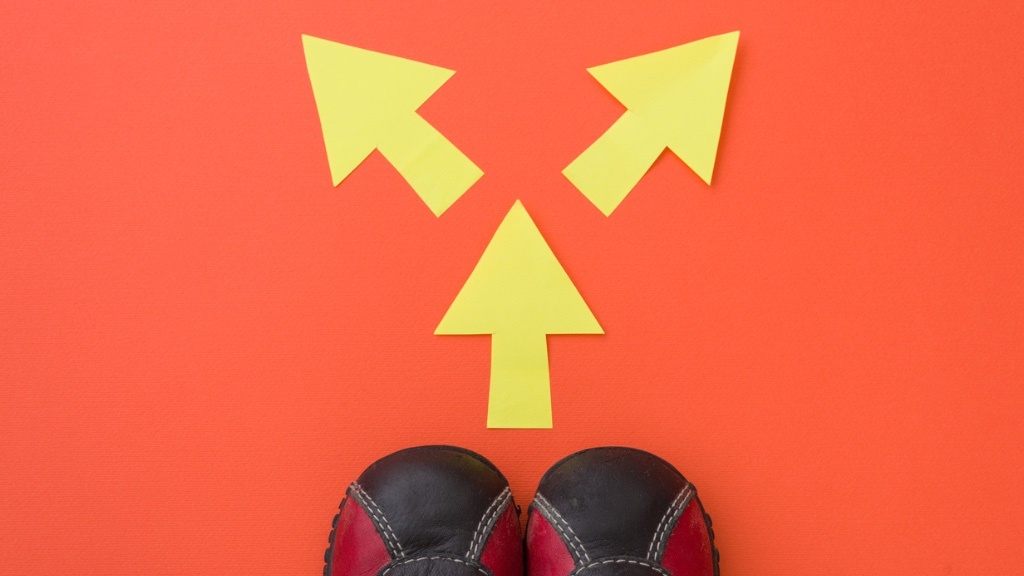 A pair of shoes is facing three yellow arrows pointing in different directions on an orange background.