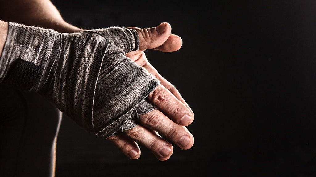 Hands wrapped in boxing bandages are clenched together against a dark background.