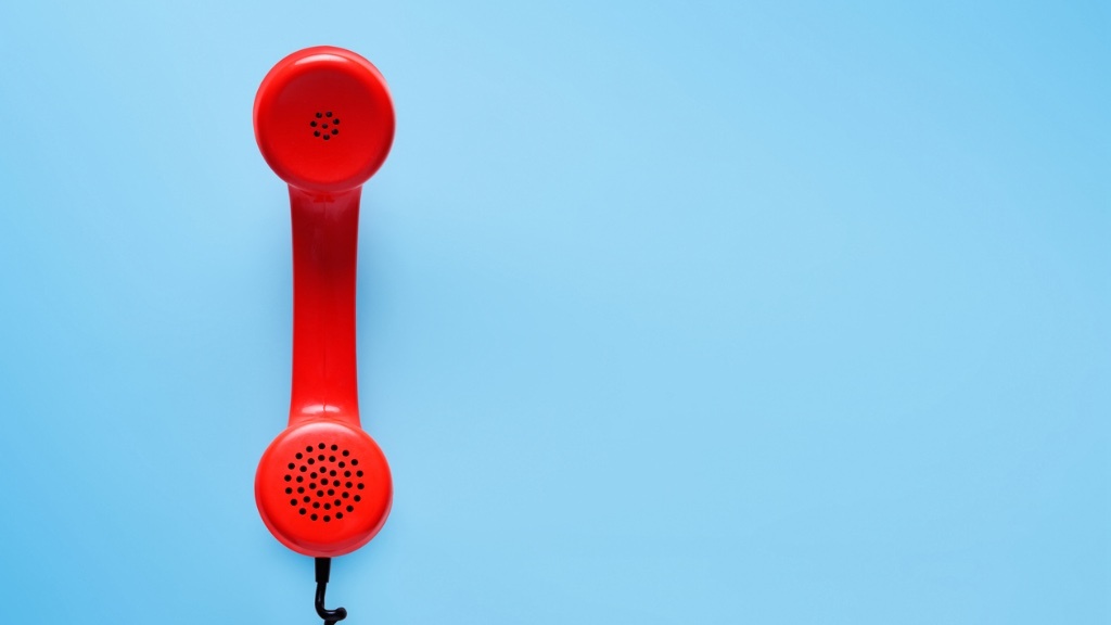 A red telephone handset is placed vertically against a light blue background.