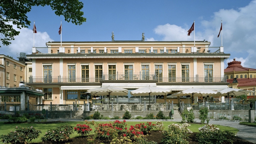 En storslagen historisk byggnad med en stor terrass och uteservering, omgiven av en välskött trädgård, närmare bestämt anrika hotell Hasselbacken i Stockholm.