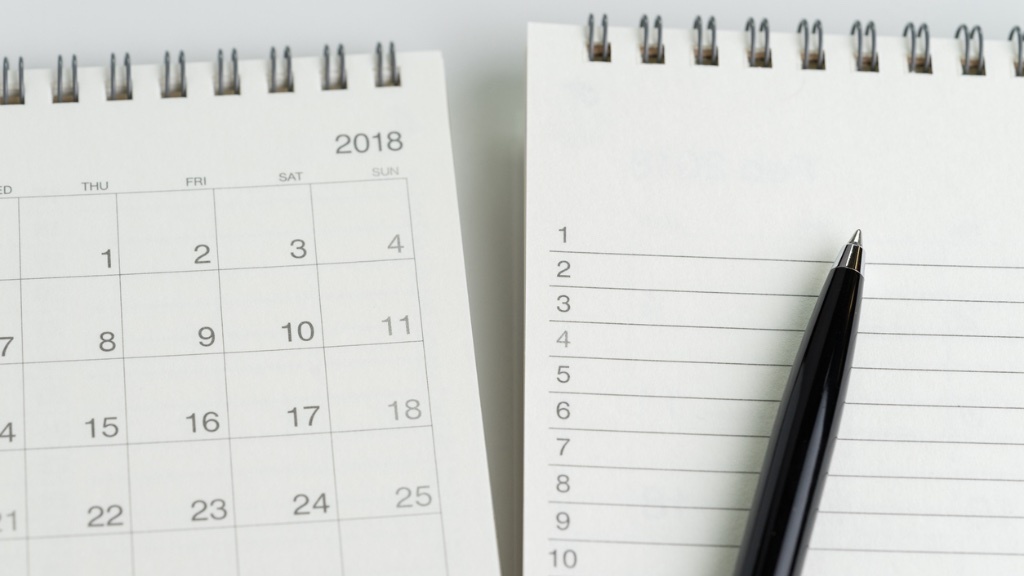 An open calendar from 2018 is placed next to a lined notepad with a black pen resting on it.