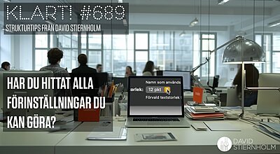 En laptop som visar inställningar för textstorlek står på ett stökigt skrivbord i ett modernt kontorslandskap med människor som arbetar i bakgrunden.